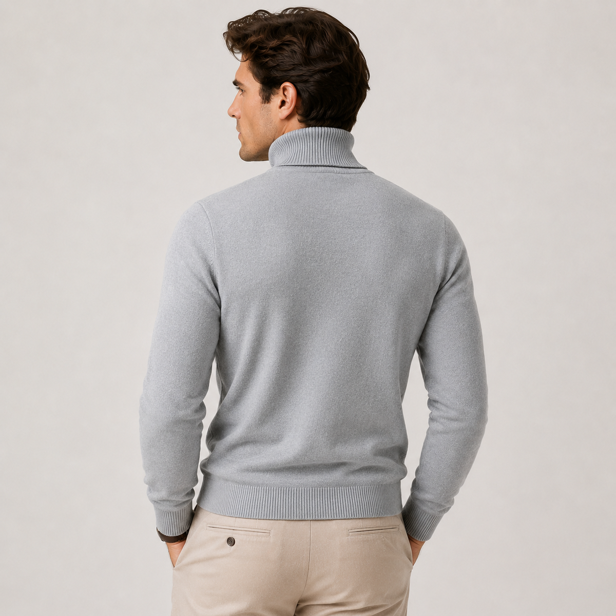 A man wearing a light gray ribbed turtleneck sweater, shown from the back, paired with beige trousers, against a plain light gray studio background.